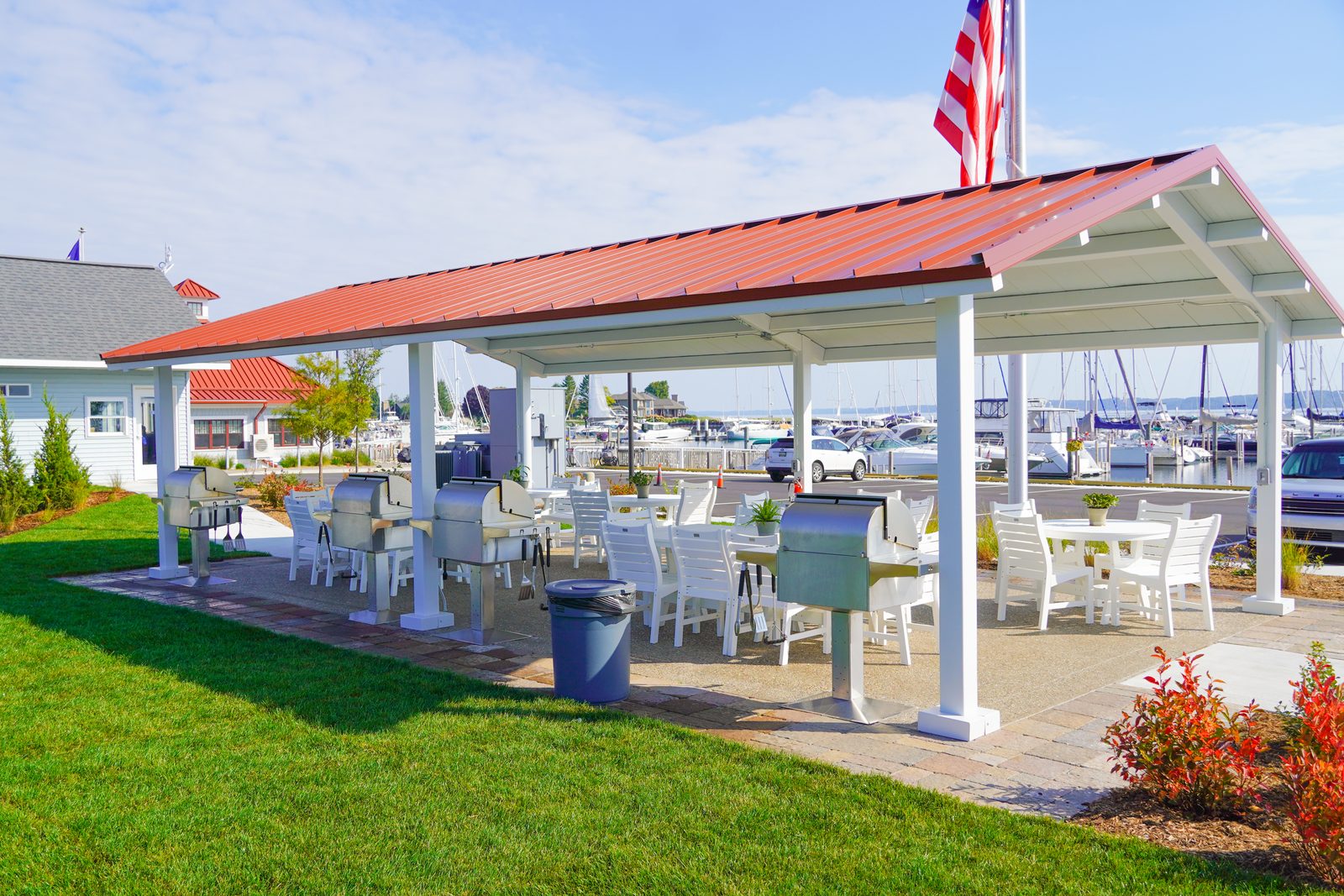 Open-air pavilion lined with white dining sets and stainless grills beside the marina.