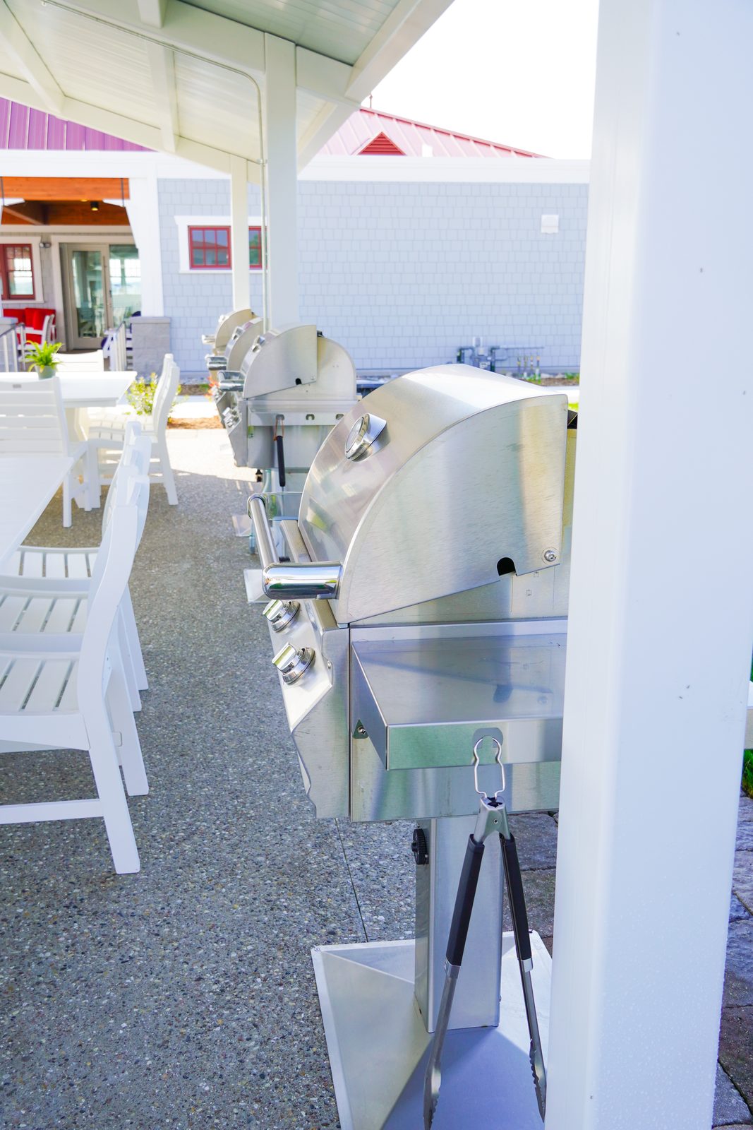 Row of stainless grills along the waterfront pavilion with sailboats in the harbor.