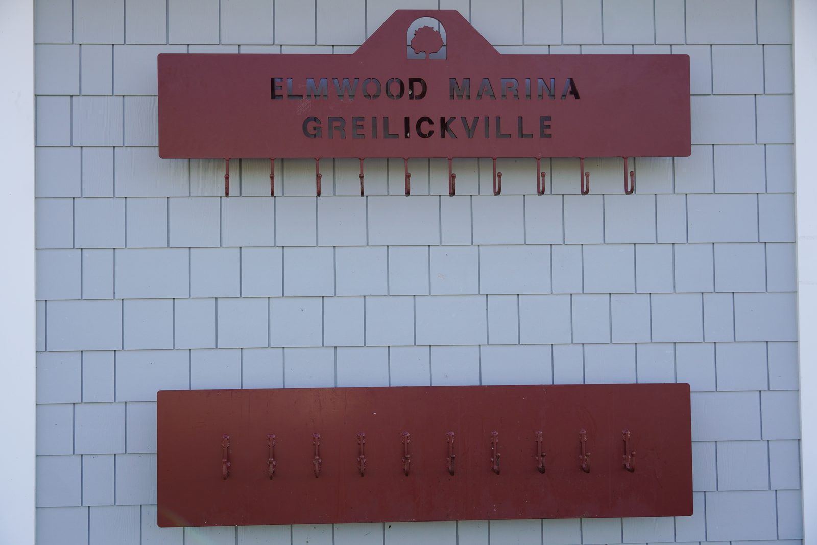 Red Elmwood Marina Greilickville sign with a row of rod and net hooks.