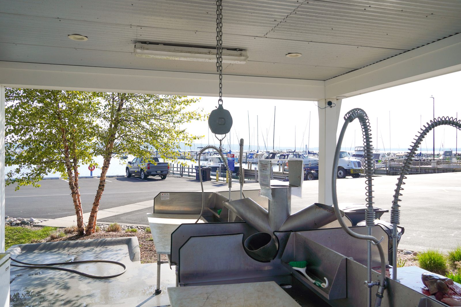 Stainless steel fish-cleaning tables under the open-air pavilion with a harbor view.